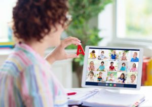 Shows a teacher holding up the letter A to her online group class